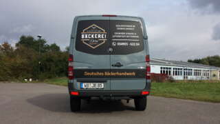 ahrzeug der Bäckerei Dorn von hinten aufgenommen, mit deutlich sichtbarer Beschriftung auf der Heckklappe – inklusive Logo, Kontaktdaten und Gestaltung im Bäckerei-Stil.